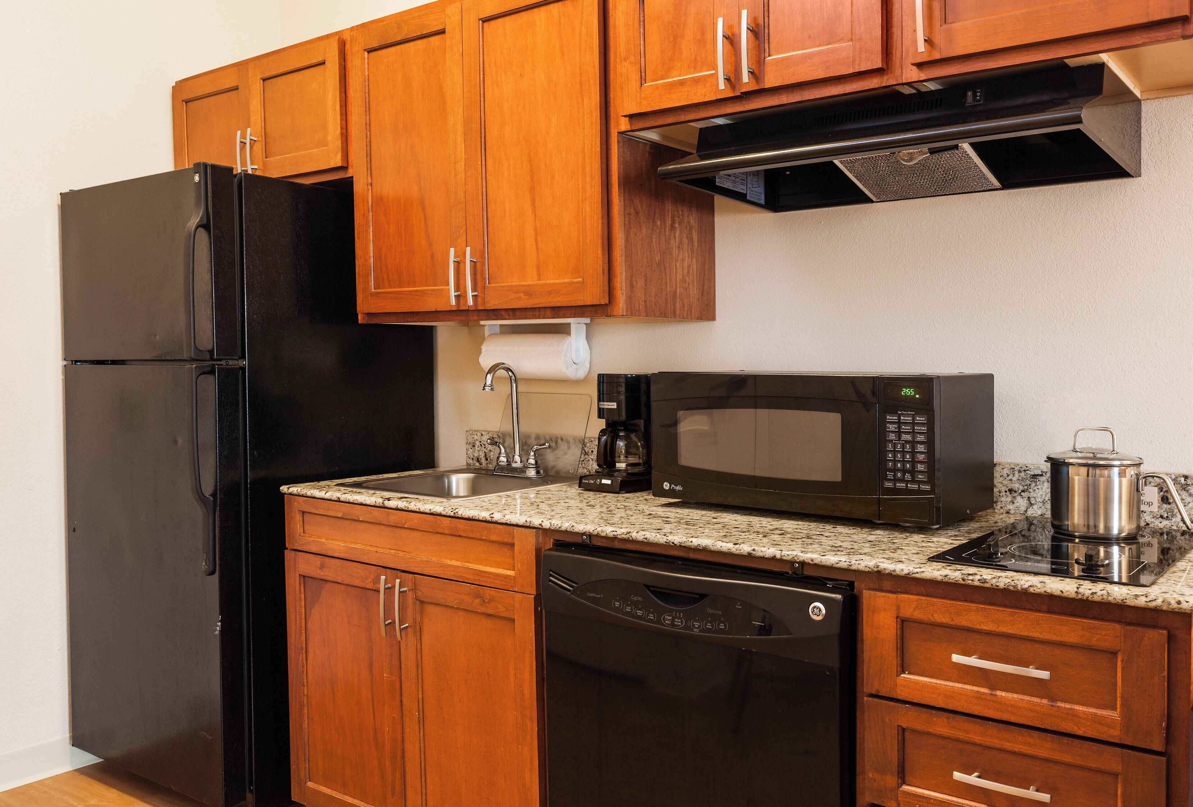 A kitchen with wooden cabinets, a black refrigerator, a microwave, a coffee maker, and a dishwasher.