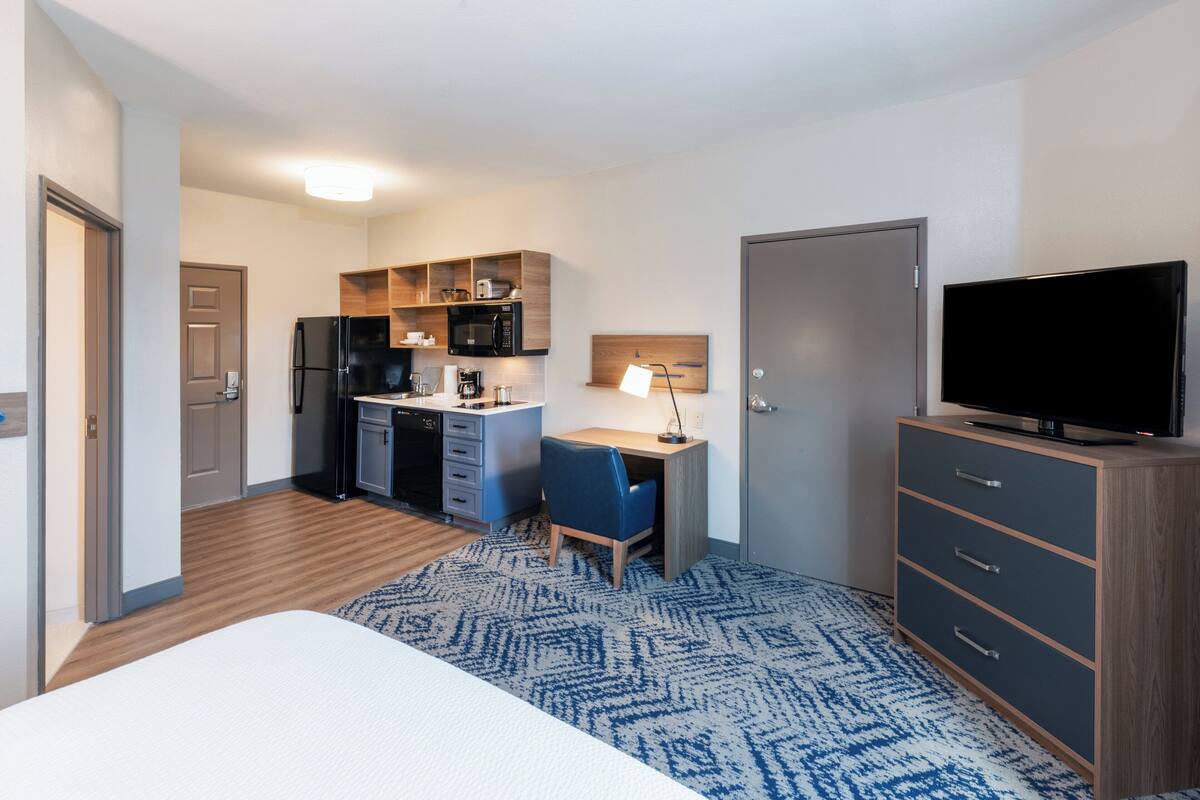 Una habitación de hotel compacta con kitchenette, una cama, un escritorio y un televisor.