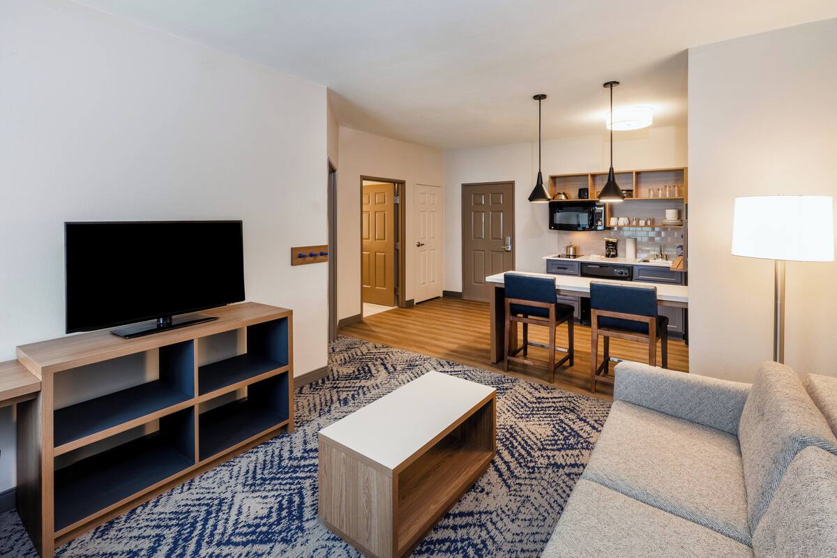 A modern living room with a flat-screen TV, wooden entertainment unit, and a patterned rug.