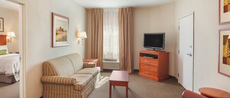 A hotel room with a striped sofa, a small table, a television on a wooden stand, a door, and a framed picture on the wall.