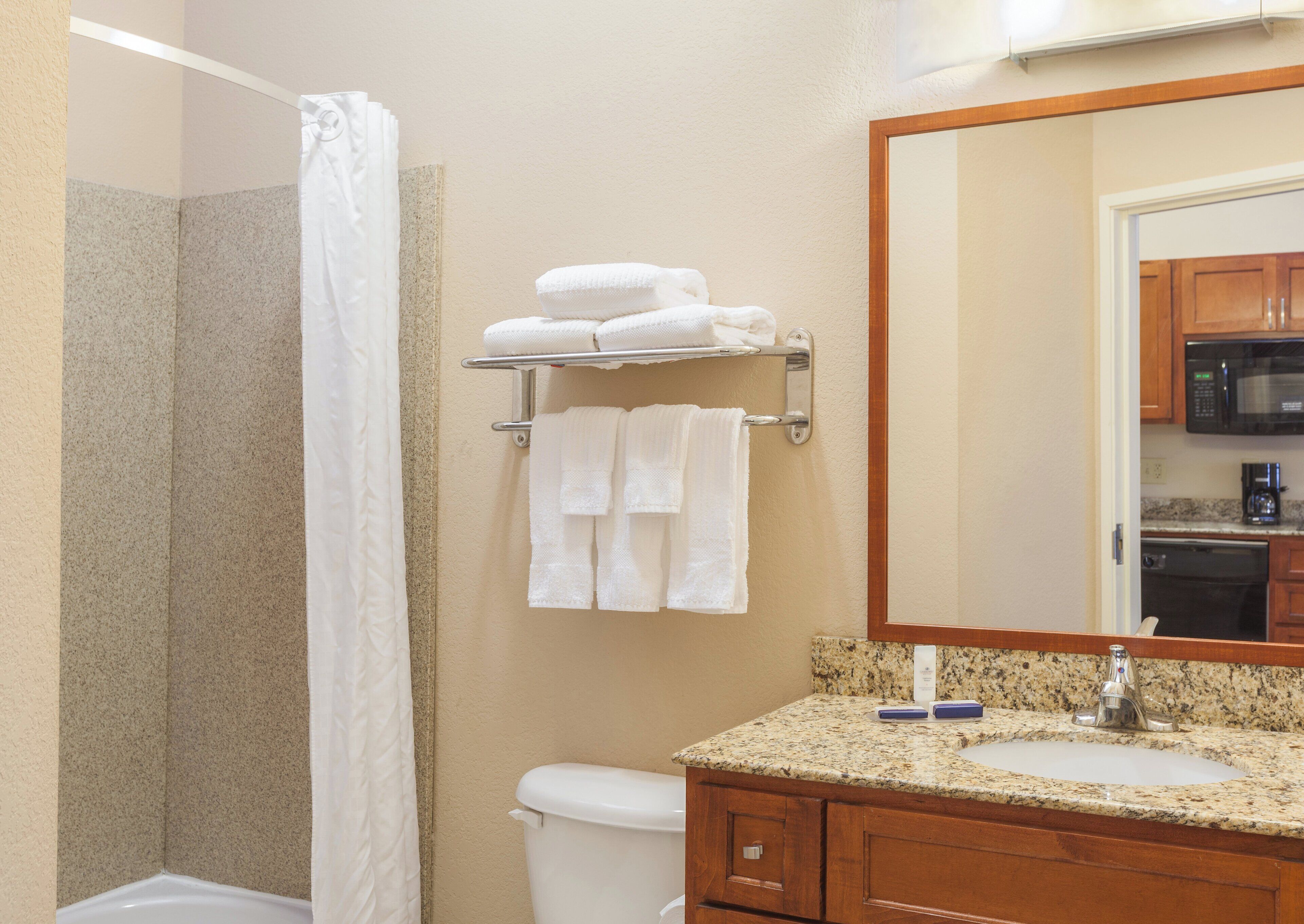 A bathroom with a shower, toilet, sink, and a towel rack with folded towels.