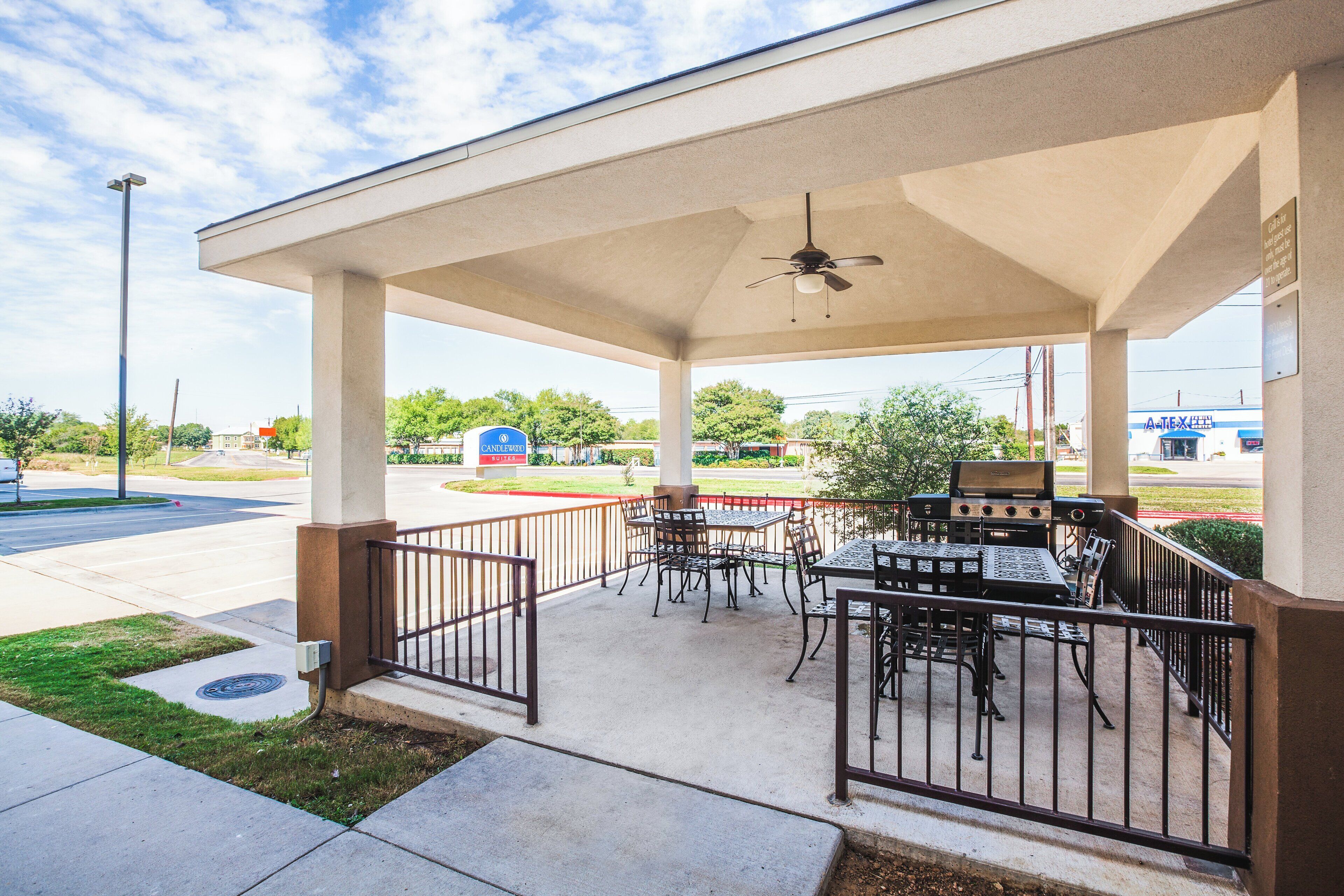 An outdoor patio with a grill and seating area, a covered walkway, and a view of a commercial area in the background.