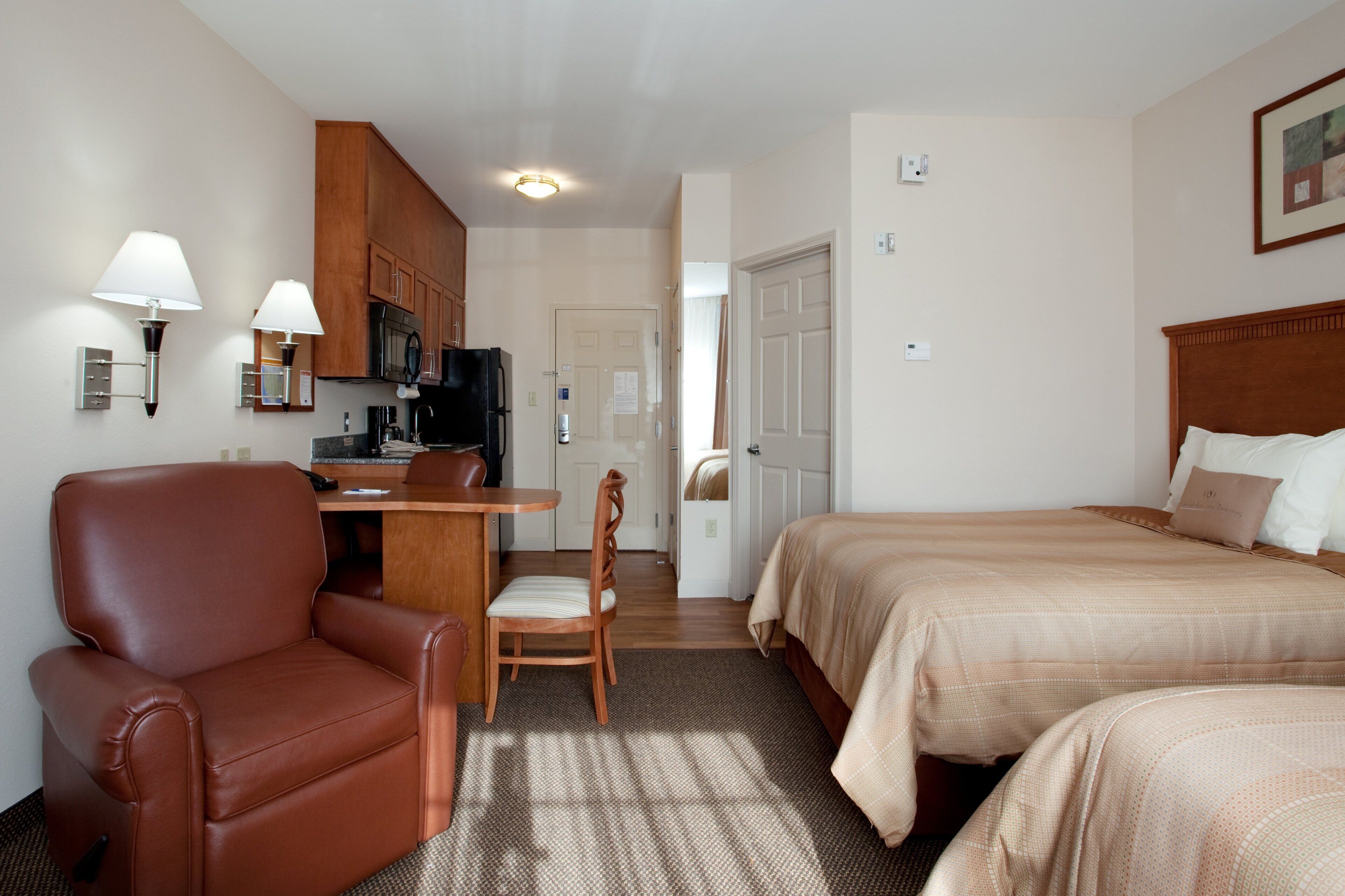 Una habitación de hotel con cama, escritorio, silla y kitchenette.