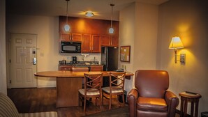 A compact living space with a kitchenette, a dining area with a bar, a leather armchair, and a small side table. - Candlewood Suites New Iberia by IHG (New Iberia)