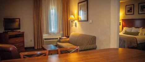 A hotel room with a wooden desk, a television, a sofa, and a bed.