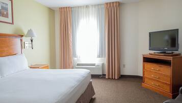 A hotel room with a bed, a television on a wooden stand, a desk with a lamp, and a window with curtains.