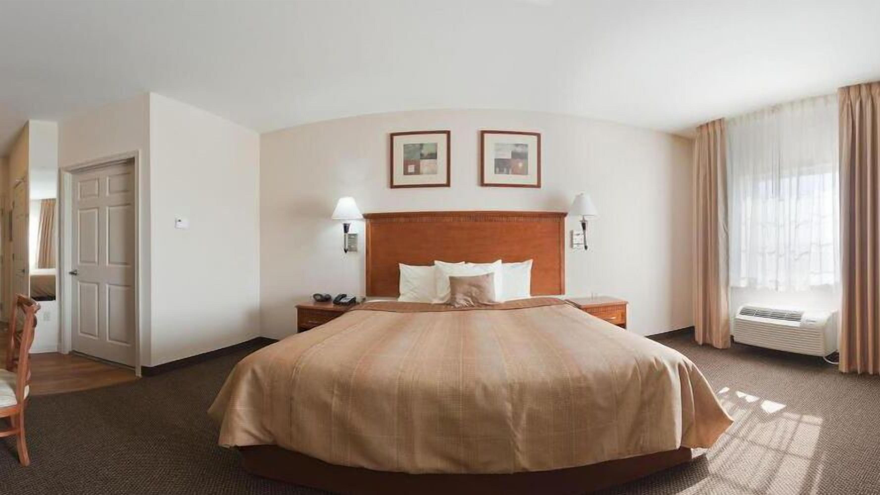 A hotel room with a large bed, two bedside tables, a chair, a door, and two framed pictures on the wall.
