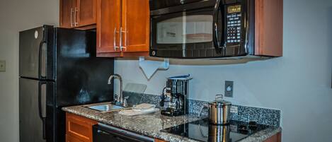 A kitchen with wooden cabinets, a black refrigerator, a microwave, a coffee maker, and a stove.