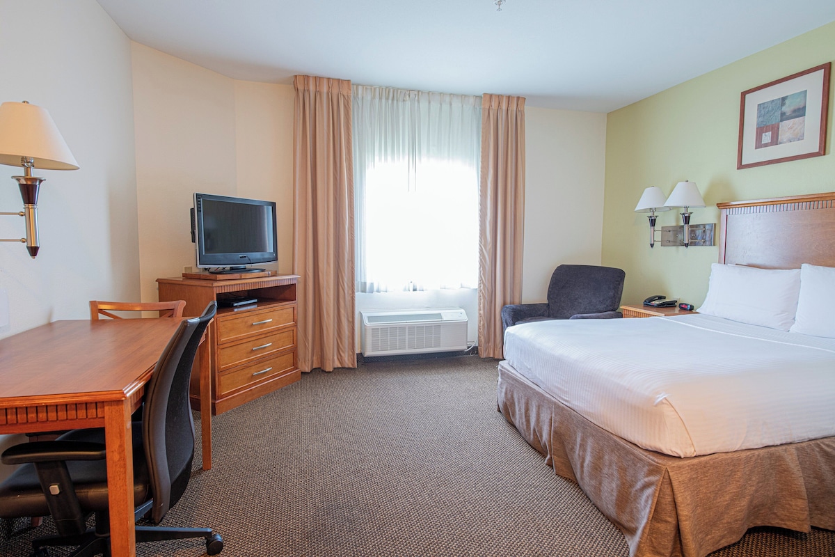 A hotel room with a bed, desk, chair, television, and a window with curtains.