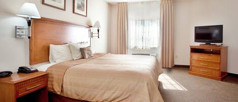 Habitación de hotel con una cama grande, televisión, escritorio con teléfono y lámpara de noche.