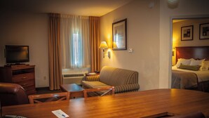 A hotel room with a wooden dining table, a sofa, a TV, a lamp, and a bed. - Candlewood Suites New Iberia by IHG (New Iberia)