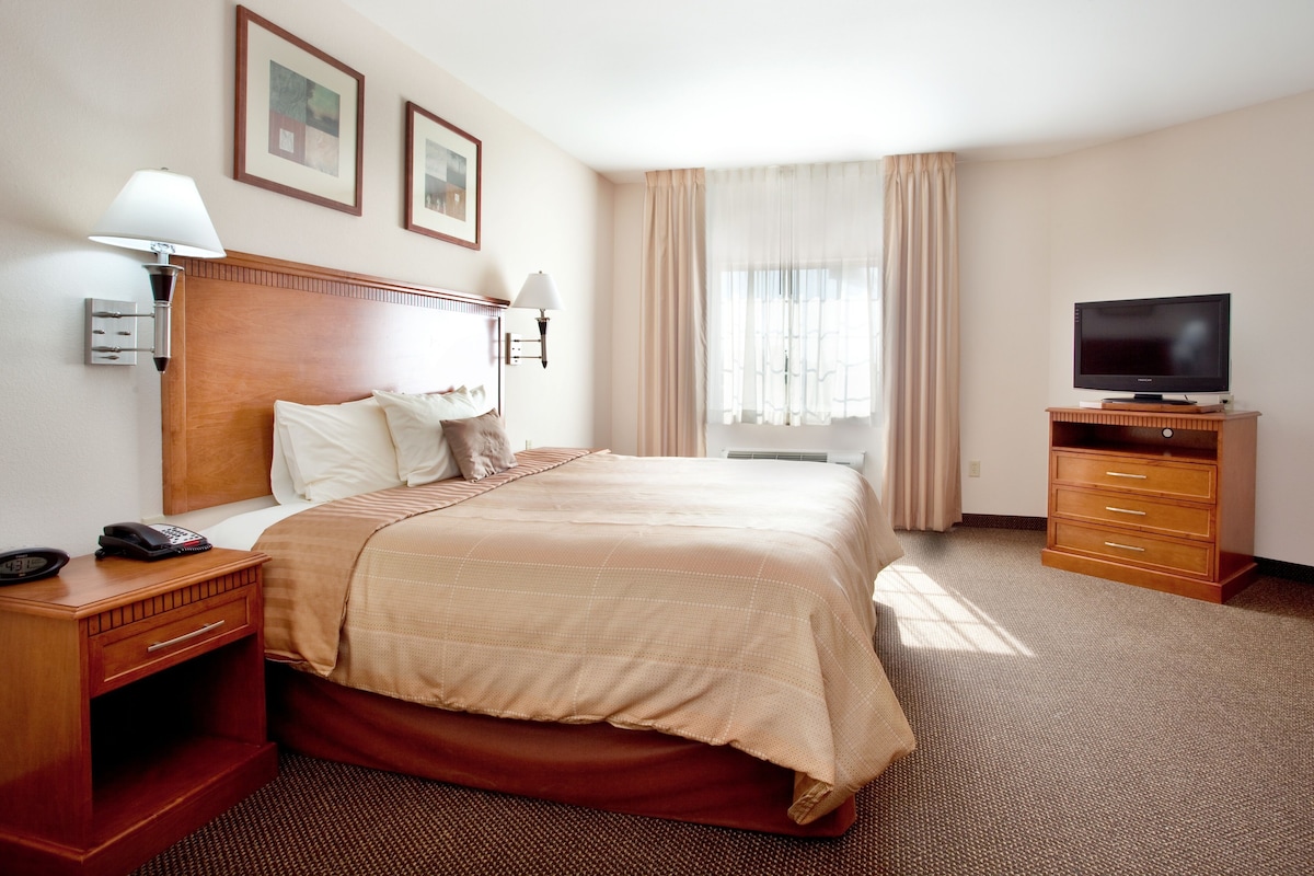 A hotel room with a large bed, bedside lamps, a television on a wooden stand, and a window with curtains.