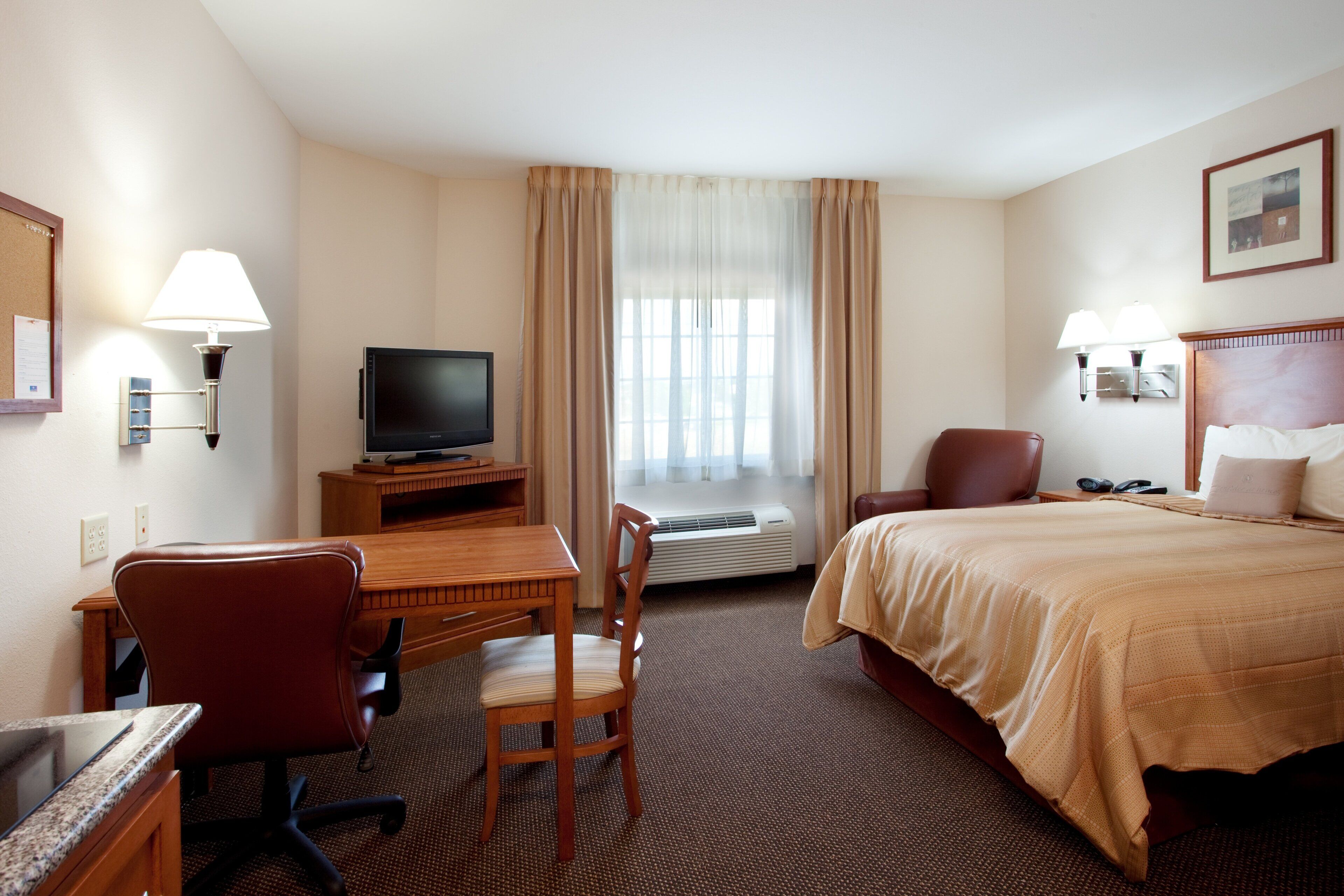 Une chambre d’hôtel comprenant un lit, un bureau avec une chaise, une télévision et une fenêtre avec des rideaux.