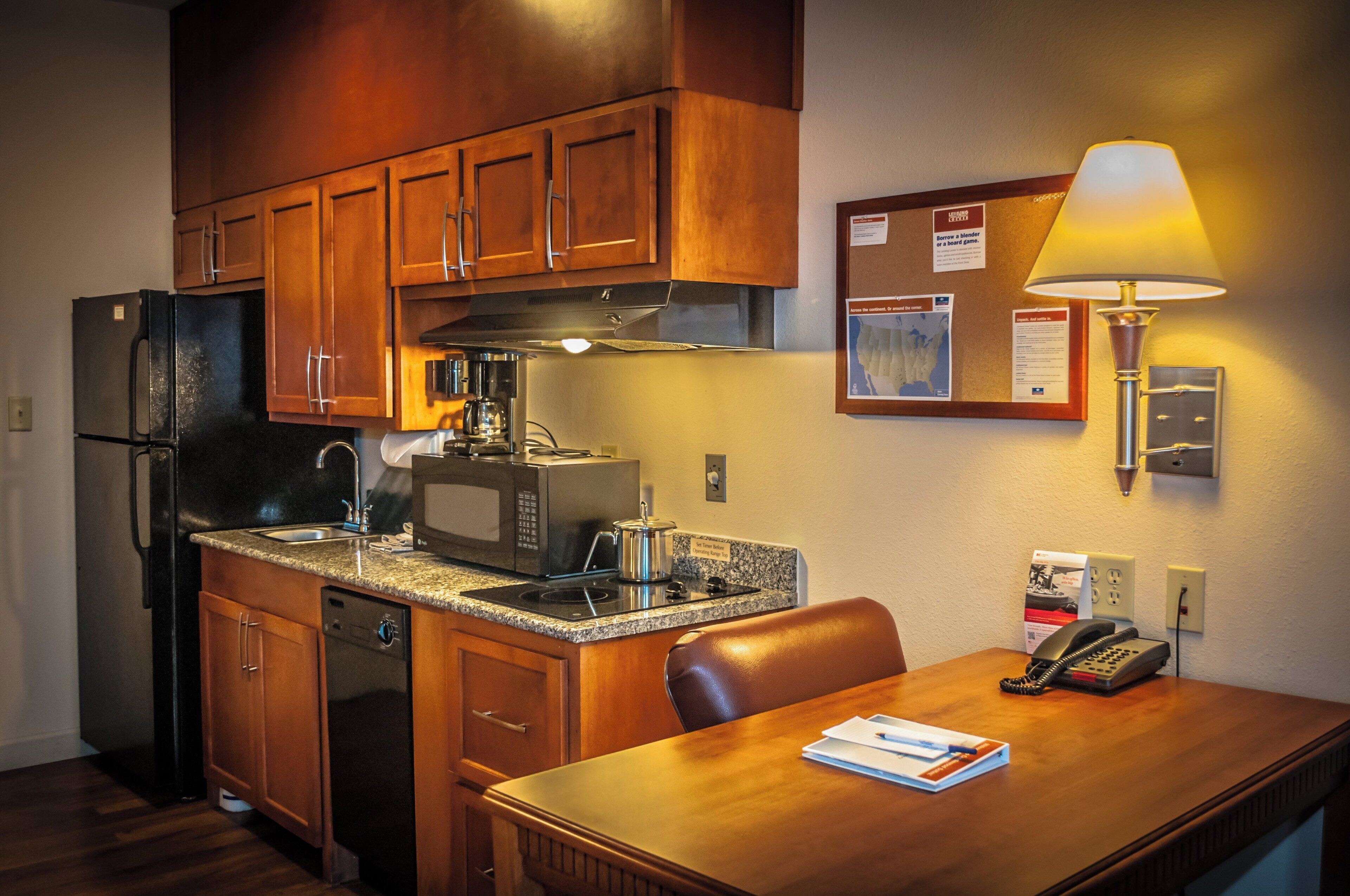 A compact kitchen with a refrigerator, microwave, stove, and a dining table with a lamp and a telephone.