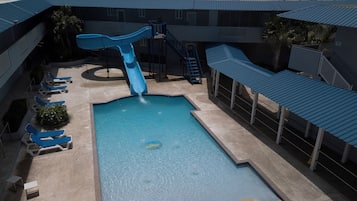 A swimming pool with a slide, lounge chairs, and a covered area.