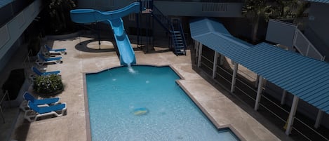 A swimming pool with a slide, lounge chairs, and a covered area.