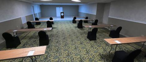 Un salón de conferencias con alfombra estampada, sillas negras y mesas de madera.