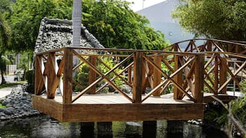 Un ponte di legno sopra uno stagno, con un muro di pietra e vegetazione sullo sfondo.