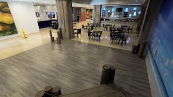 Un espacio interior amplio con piso de madera pulida, una zona de bar con mostrador y asientos, y un cuadro grande en la pared.