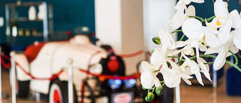 A vintage car on display with a red rope barrier, surrounded by white orchids.