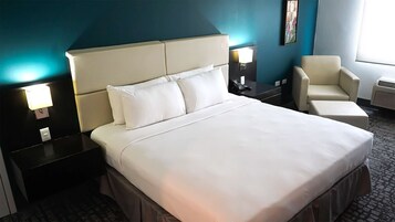 A hotel room with a large bed, two bedside tables, a chair, and a nightstand with a lamp.