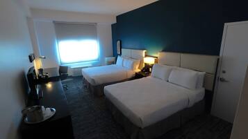 Ein Hotelzimmer mit zwei Betten, einem Schreibtisch, einem Stuhl, einem Fenster mit Jalousien und einer Tür.