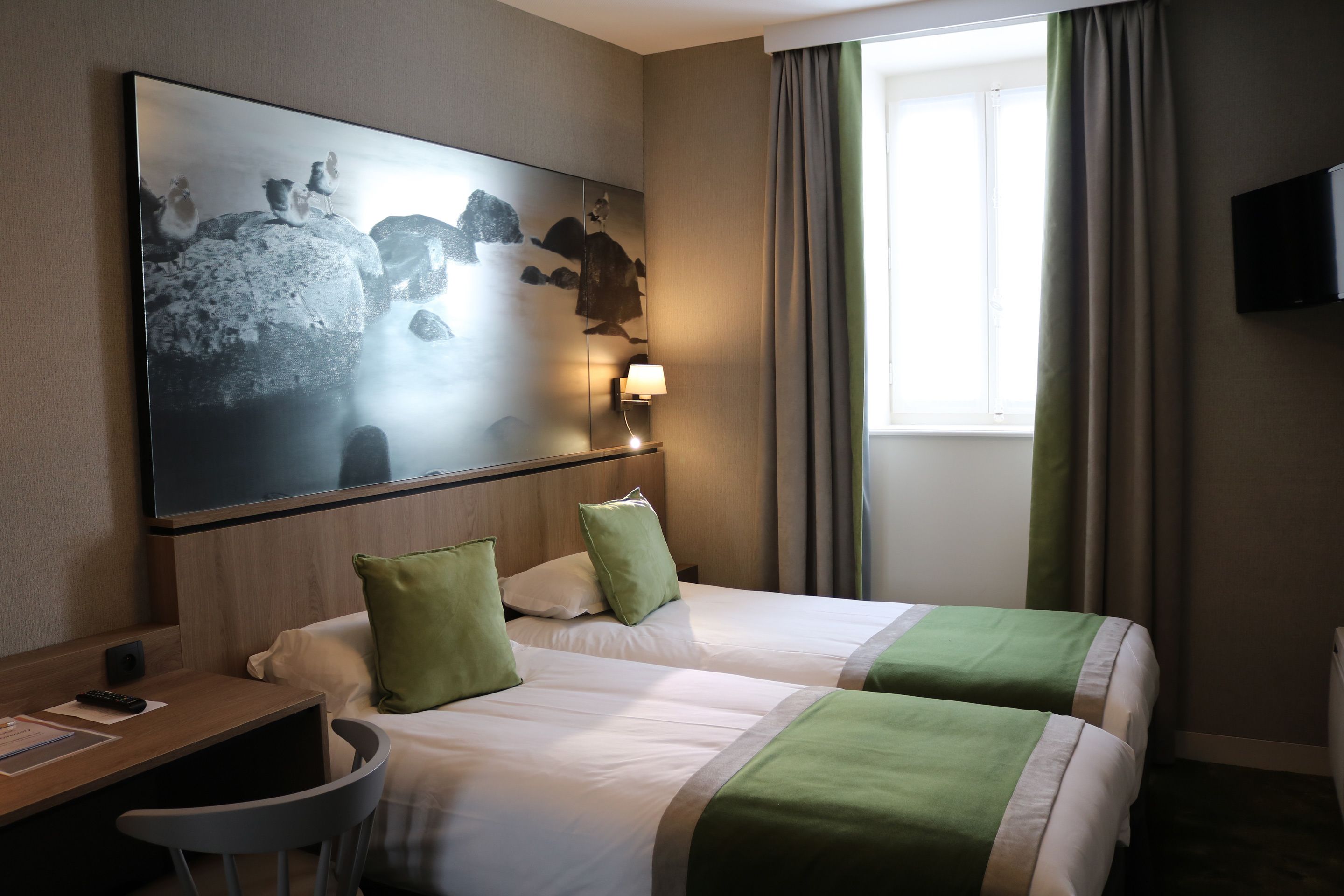 Una habitación de hotel con dos camas, un escritorio, una silla, un televisor y una obra de arte grande en la pared.
