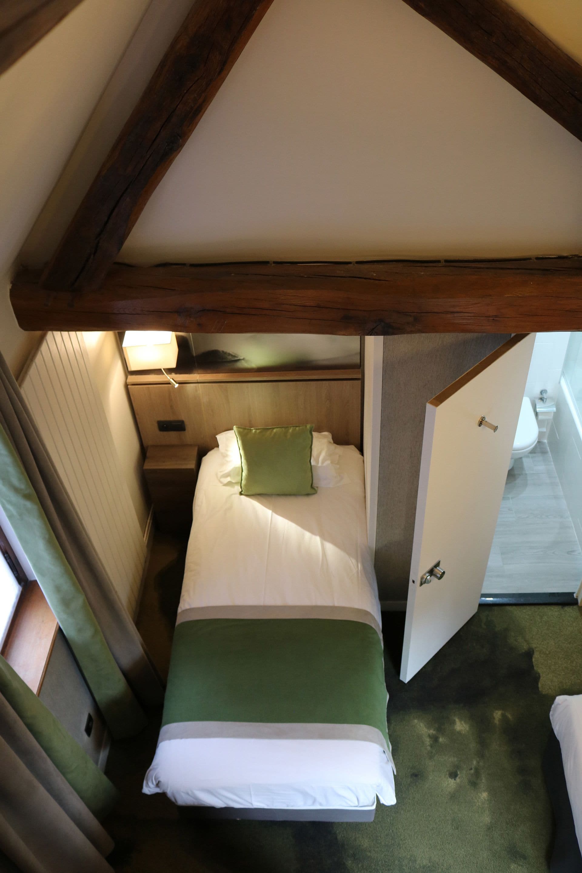 A small, cozy room with a single bed, a nightstand, a lamp, and a door leading to a bathroom.