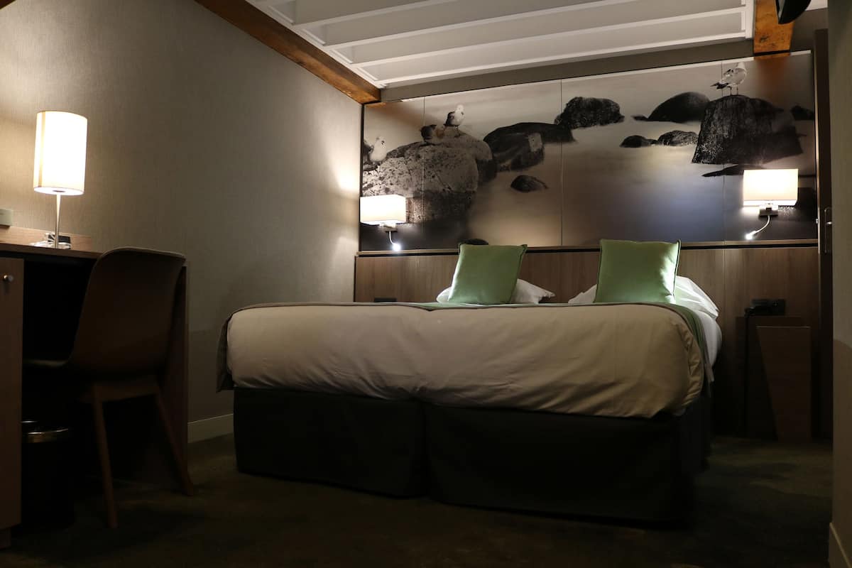 Ein Hotelzimmer mit einem Bett, einem Schreibtisch und einem Stuhl. Über dem Bett befindet sich ein Wandbild.