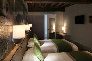 Habitación de hotel con dos camas, cabecero de madera, espejo, televisor y lámparas de noche.