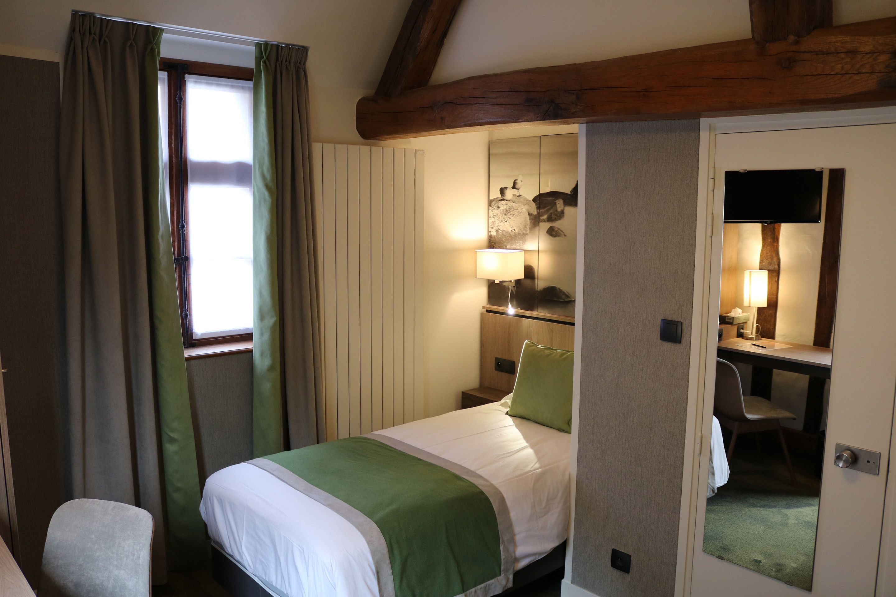Una habitación de hotel con cama, escritorio, silla y espejo.