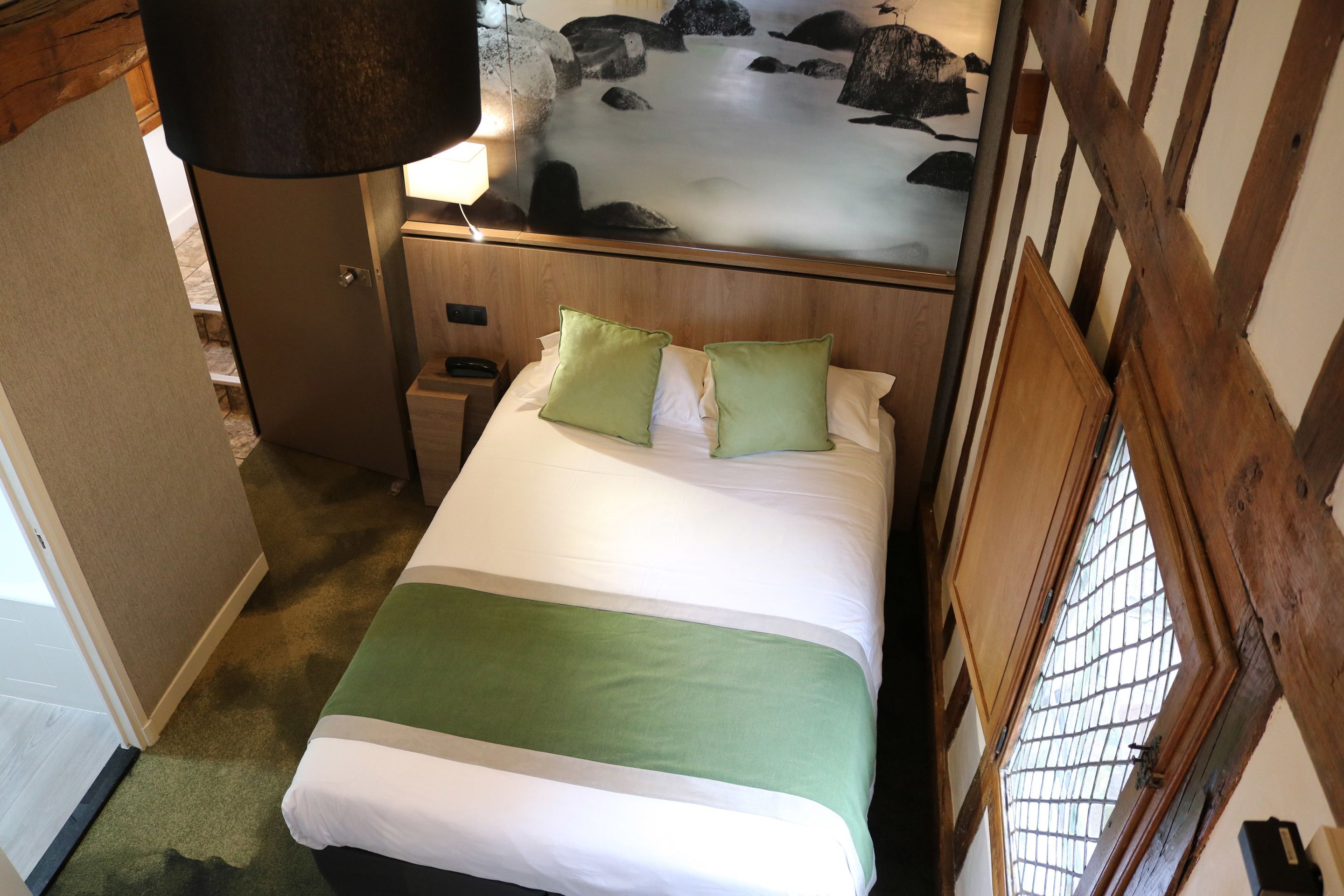 A hotel room with a bed, a nightstand, a lamp, and a mural on the wall.