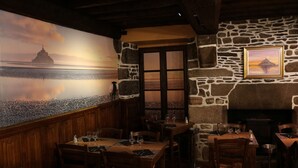 Un restaurante con paredes de piedra, mesas de madera y un mural que muestra un atardecer sobre un cuerpo de agua.