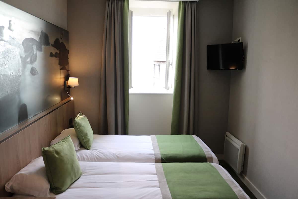 Ein Hotelzimmer mit Bett, Kissen, einem an der Wand befestigten Fernseher und einem Fenster mit Vorhängen.