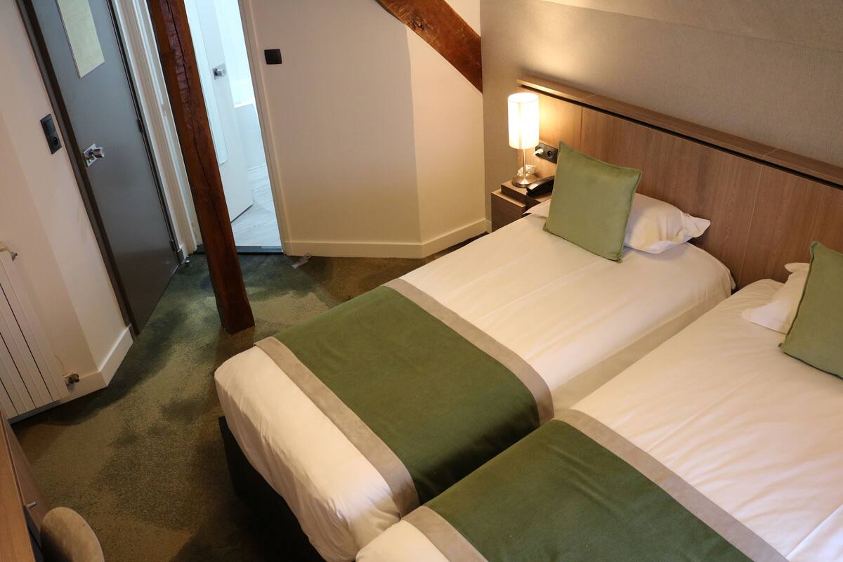 Ein Hotelzimmer mit zwei Betten, einem Nachttisch mit Lampe und einem Holz-Kopfteil.