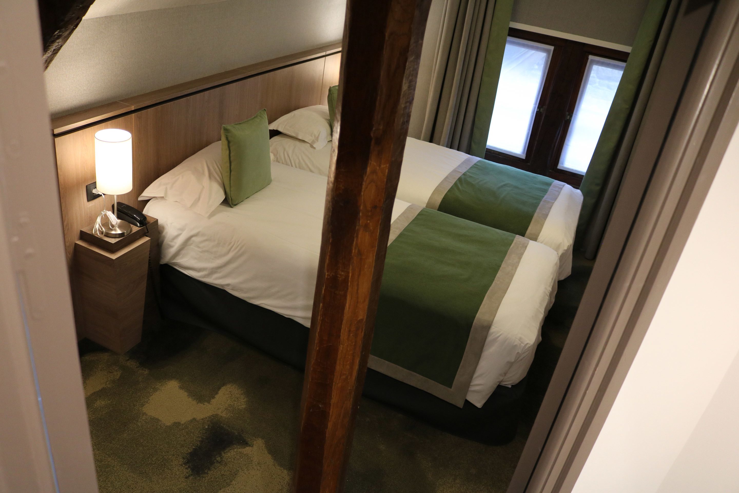 Een hotelkamer met een bed, een nachtkastje met een lamp en een raam met gordijnen.