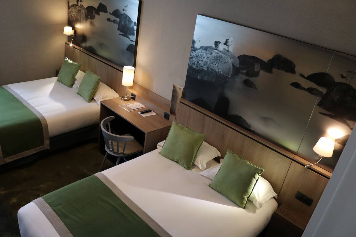 Zwei Einzelbetten mit grüner Bettwäsche, ein Schreibtisch und ein Stuhl in einem Hotelzimmer.