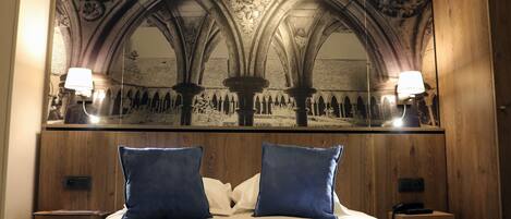 A hotel room with a large mirror reflecting a gothic ceiling, a bed with blue pillows, and bedside lamps.