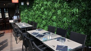 Un área de comedor al aire libre con mesas dispuestas para dos, rodeada de exuberante follaje verde.