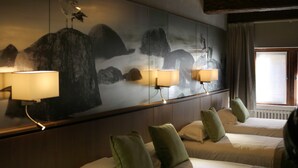 Una habitación de hotel con un mural grande en la pared, dos camas con almohadas verdes y una ventana con cortinas.