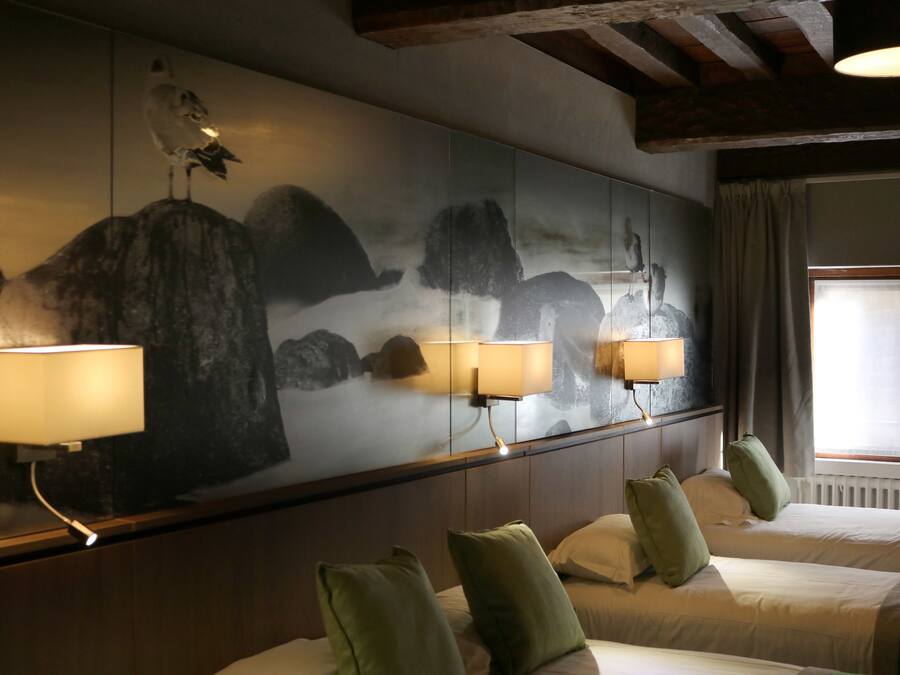 Une chambre d’hôtel avec une grande fresque murale, deux lits avec des oreillers verts et une fenêtre avec des rideaux.