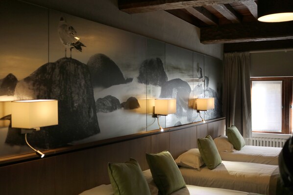 A hotel room with a large wall mural, two beds with green pillows, and a window with curtains.