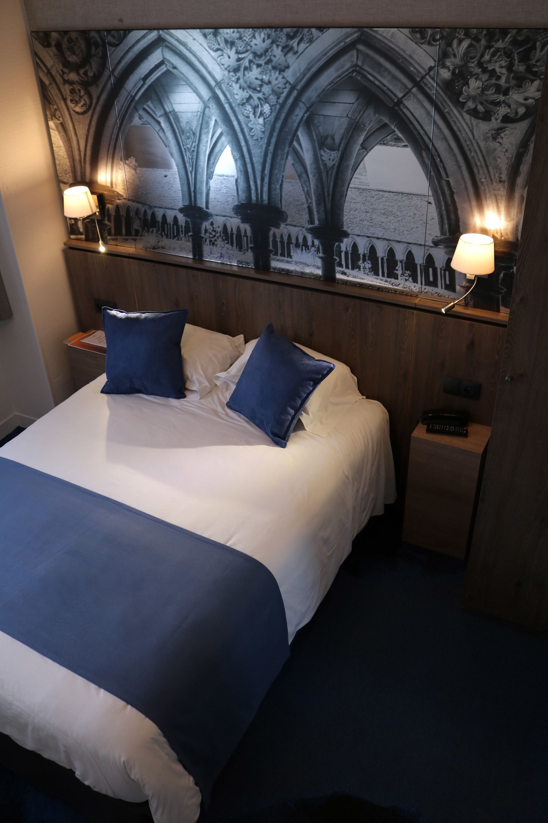 A hotel room with a large bed, two bedside lamps, a nightstand, and a decorative wall mural.