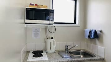 Uma cozinha compacta com micro-ondas, chaleira, pia e janela.