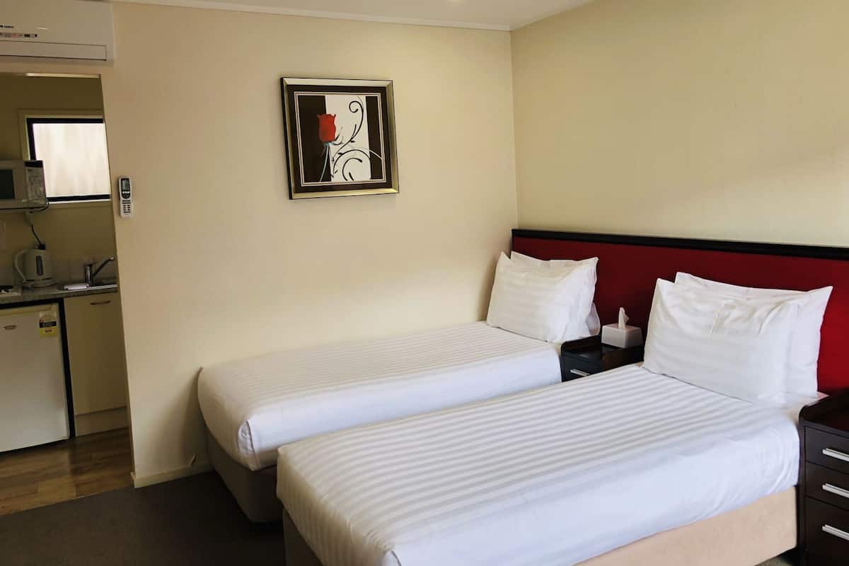 Habitación de hotel con dos camas, un cabecero rojo, una kitchenette pequeña y una obra de arte enmarcada en la pared.