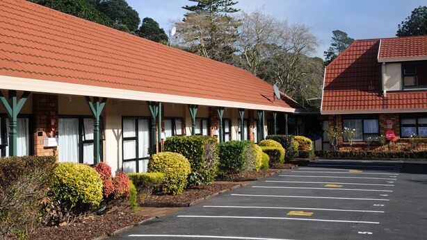A motel with a red-tiled roof, a parking lot, and neatly trimmed bushes. - Tudor Court Motor Lodge (Auckland)