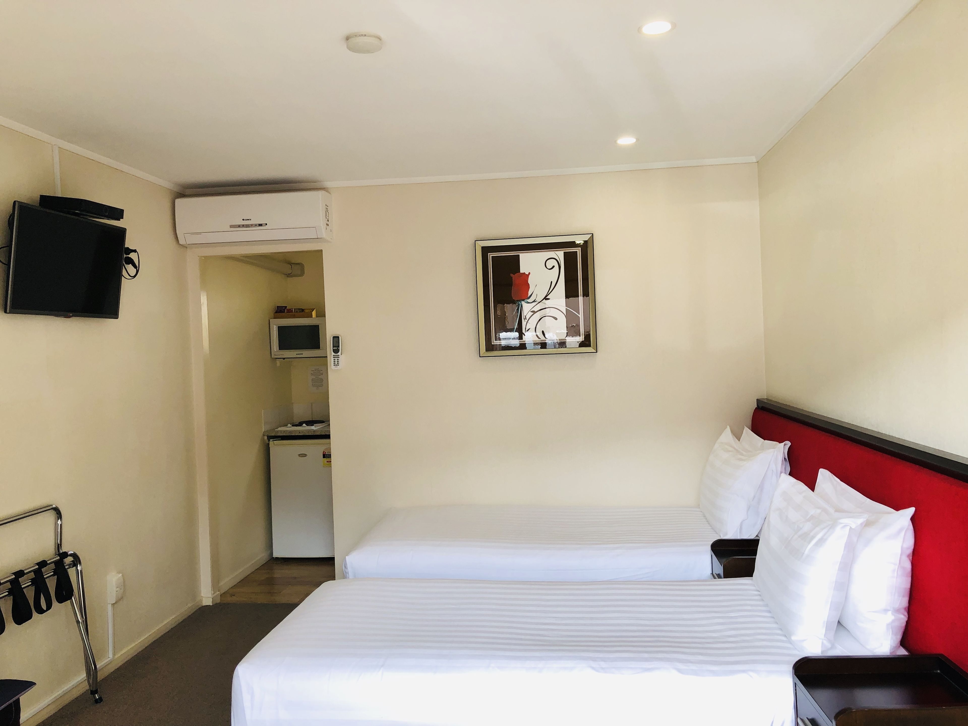 A hotel room with two beds, a TV mounted on the wall, a microwave, and a small kitchenette.