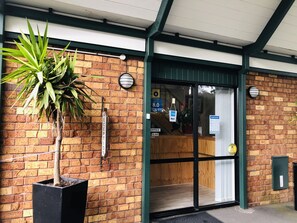 A reception area with a brick wall, a potted plant, and a glass door. - Tudor Court Motor Lodge (Auckland)