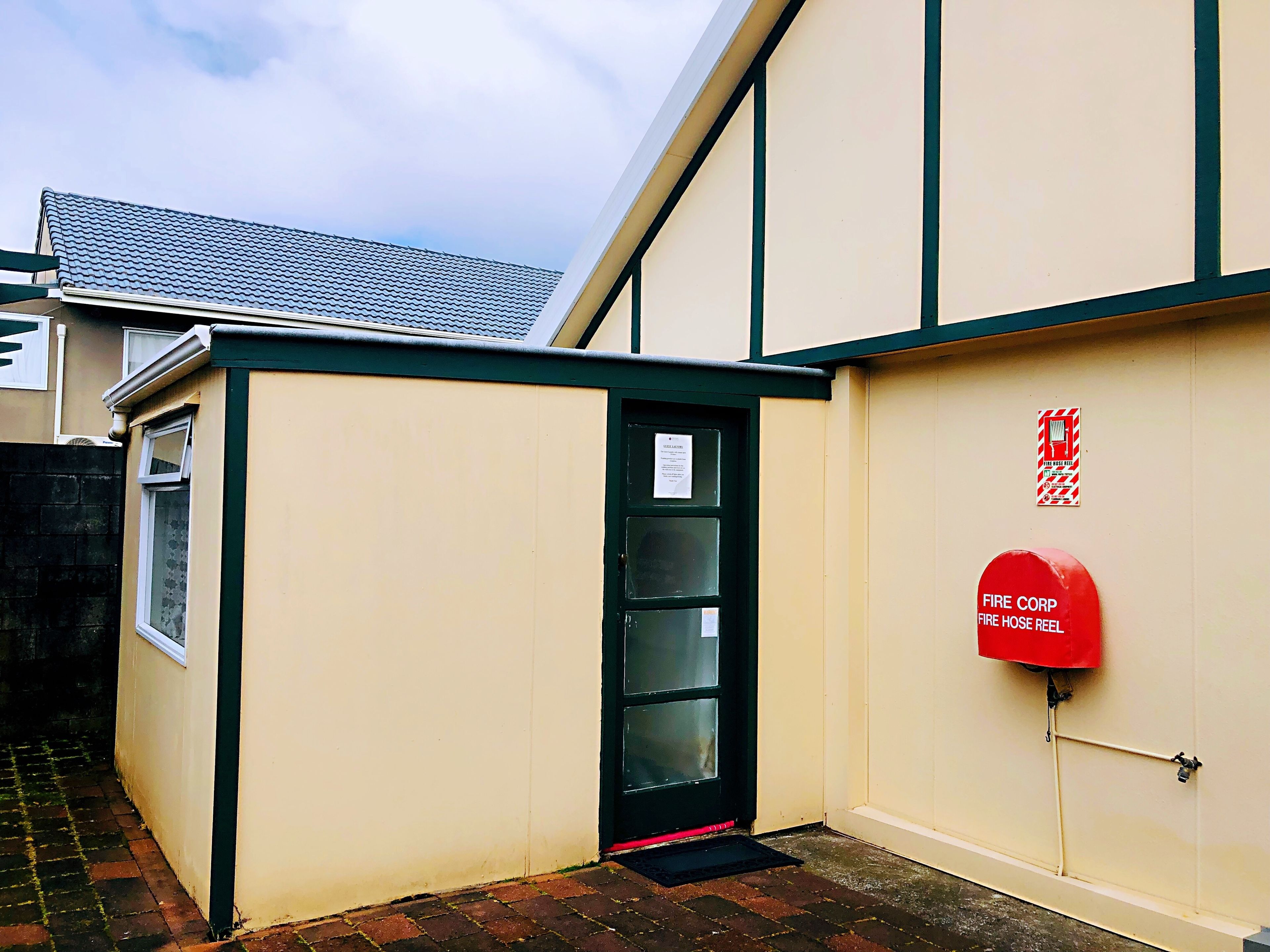 A building with a fire hose reel mounted on the wall, a fire safety sign, and a door with a window.