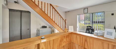 A reception area with a wooden staircase, a desk with a computer, a chair, and a window with a view of the outside.